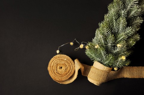 Preparation of decorations for winter celebrations. Artificial Christmas tree, natural jute fiber strip, dark background, cozy lighting