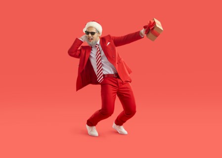 Cool energetic man in santa hat having fun and dancing with christmas gift in hand.