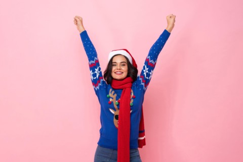 Festive portrait of joyful woman wearing Christmas sweater and hat raising hands up in pink color isolated background studio shot