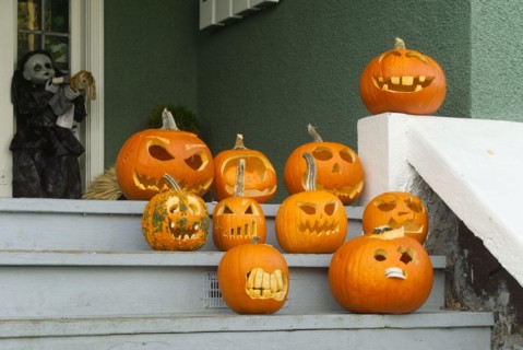 Humorous carved Halloween pumpkins displayed on the wooden front stairs of a house