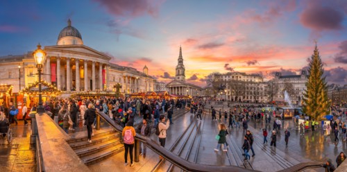 London, UK - November 25, 2023: Twilight at Trafalgar Square with golden sunset hues, reflecting on wet streets—capturing London's vibrant evening cha