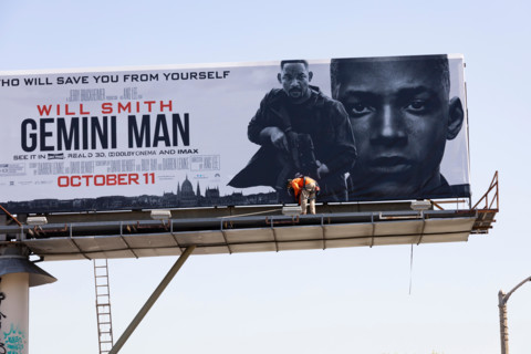 Huge billboard for the film Gemini, starring Will Smith, being erected by a man in orange hi viz jacket above the street. Los Angeles, California, USA
