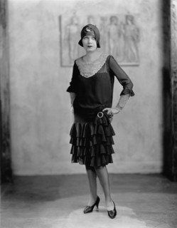 Young woman in a 'flapper' dress and cloche hat posing for portrait with hands on hips. Circa 1922