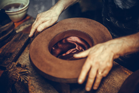 Close up shot of a hatter's hands, manufacturing a hat.