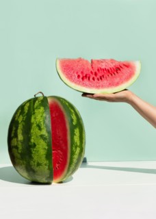 Ripe fresh watermelon on neo mint colored background. Woman's hand holding slice of watermelon.Creative minimal summer fruit concept.