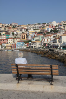 man sitting on bench in the port at parga, greece