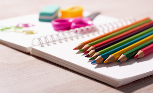 Close up of wooden crayons and other school supplies on blank note book on wooden desk