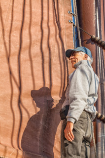 Senior man on a sailboat helps to hoist the sail. Adventure travel on a tall ship schooner. Concept for staying healthy in active retirement.