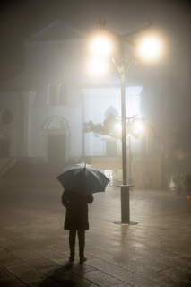 Person with umbrella standing under street lamp in front of the duomo in rain and fog at night, Ravello, The Amalfi Coast, Campania, Italy, Europe