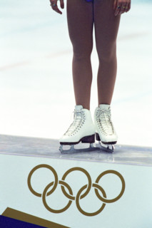 Detail of female figure skater standing atop the podium with the Olympic Rings.