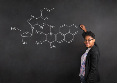 South African or African American woman teacher writing science on chalk black board background