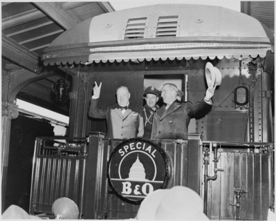 Photograph of President Truman waving his hat and Winston Churchill flashing his famous V for Victory sign from the rear platform of a special Baltimore & Ohio train (evidently en route to Fulton, Mis...
