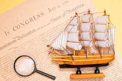 Ship made of wood and fabric handmade on the background of an excerpt from a copy of the document of 1776 on the signing of the independence of