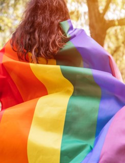Lesbian woman wearing an LGBTQ flag, symbol for the homosexual community, as a cape. Gay rainbow colors flag for pride month and the celebration day o