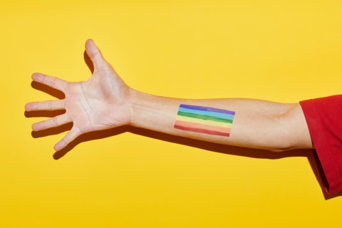 Vibrant yellow shot of arm with rainbow flag tattoo as symbol for pride month LGBTQ