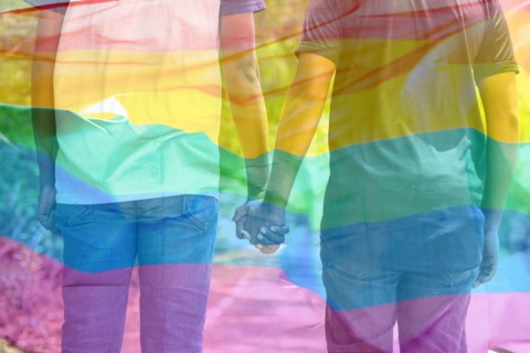 Double exposure shot of flying lgbtq flag with couple joining hands in background - concept of pride month celebration, freedom and quality