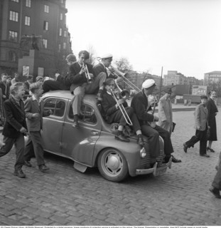The student celebration in 1954. The students celebrate their completed matriculation and a band sits on top of a Renault 4CV which sags heavily under the weight of the orchestra. They pass the Aviato...