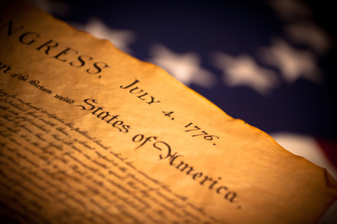 The Declaration of Independence in front of a Betsy Ross American flag, focus is on July 4, 1776 then falls off quickly