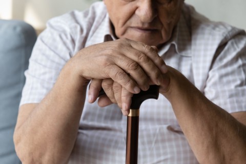 Closeup cropped old man holding hands on walking cane.