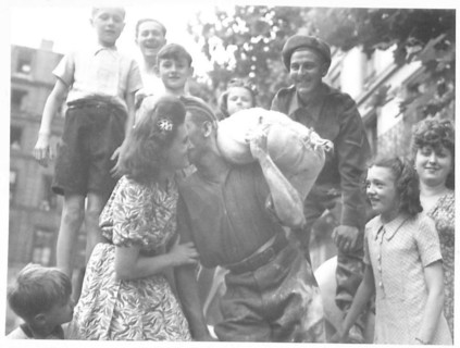 A British soldier unloads flour in the Les Halles market in Paris while pausing to interact with a young French girl, part of post-liberation food supplies.