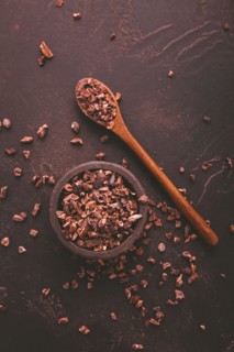 Organic cocoa nibs and cocoa beans in a bowl on brown background