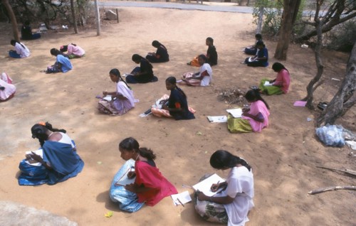 Young students sitting on the ground writing during an outdoor lesson in tamil nadu, India