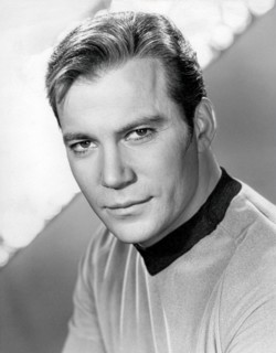This 1960s black and white publicity still features William Shatner as Captain James T. Kirk from the original Star Trek television series. He is depicted in his iconic gold Starfleet uniform, looking...