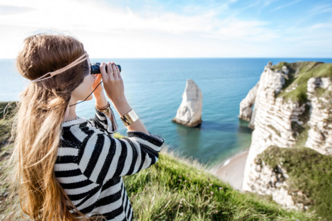 Young woman watching with binoculars on the famous rocky coastline near Etretat town in France