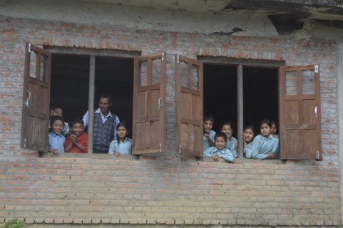 Nepalese children looking out of their classroom 's window together with their teacher curious for who is in their non touristy small village, Panauti.