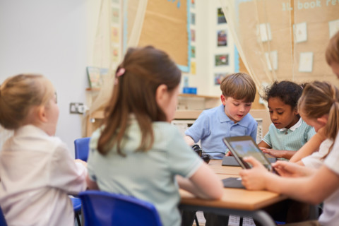 Schoolboys and girls looking at digital tablets in class at primary school