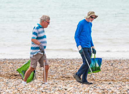 Pair of good samaritan volunteer men picking up litter from a beach in the UK.