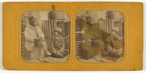 Man in tall hat and sheepskin coat with another man in cap seated up against a crate; 1855 - 1860; Hand-colored Albumen silver