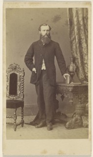 Full-bearded man, standing, with hand on book resting on table; Schwarzschild & Co; 1860s; Albumen silver print