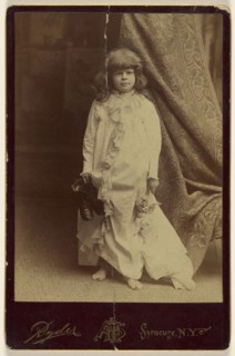 Ethel Butter in white dressing gown, holding pair of shoes and a doll, standing; Philip S. Ryder American, active 1870s - 1920s