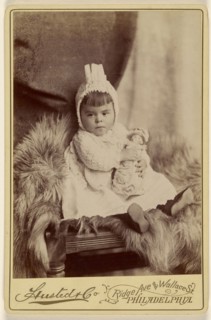 Baby girl in bonnet, seated, holding a doll; A. Husted & Company; about 1880; Albumen silver print