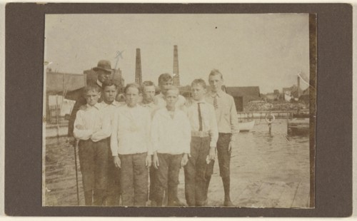 Eight young men standing on a dock near a river, with a man wearing a hat; 1875 - 1885; Albumen silver print