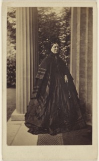 elderly woman standing outside near column at house entrance; J.G. & E.G. Short, British, 1865 - 1875; Albumen silver print