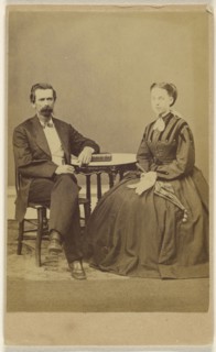 couple, both seated at a table with a book on top; the man has a bushy moustache; S.G. Sheaffer & Company; 1870 - 1875; Albumen