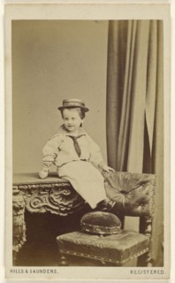 little boy seated on a table, wearing a straw hat with a Speedwell banner; Hills & Saunders, British, active about 1860 - 1920s