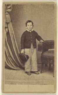 little boy standing, holding his cap, with hand on chair back with tassels; H. Jaeger & Company; 1865 - 1875; Albumen silver