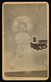 Child  spirit  with photograph and figurine on table; William H. Mumler, American, 1832 - 1884, Boston, Massachusetts, United