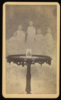 Five  spirits  in background with a photograph at center of table with a doily; William H. Mumler, American, 1832 - 1884