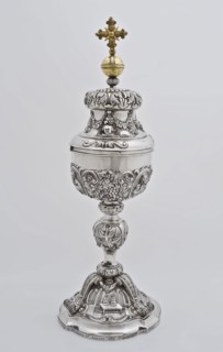 Silver ciborium with lid on which gold-colored cross, ciboric liturgical container holder gold silver, driven chased