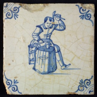 Occupation tile, blue with seated blacksmith with raised hammer and anvil, corner motif oxen head, wall tile tile sculpture