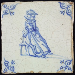 Figure tile, blue with lady sitting on stool, with hat, wide collar and apron, corner pattern ox head, wall tile tile sculpture