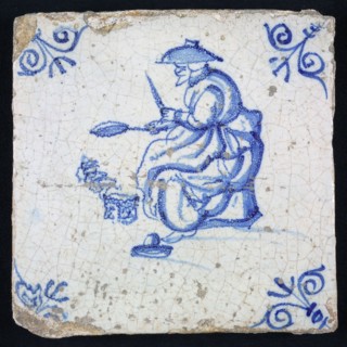 Tile, blue with woman sitting with frying pan in her hand, corner motif-shaped ox-head, wall tile tile sculpture ceramic