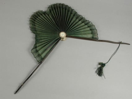 Parasol fan, two thin dark brown wooden legs, leaf shaped fan leaf of green silk with green edge around it, legs knots, cord and