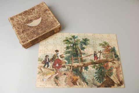 Wooden jigsaw puzzle with landscape with mother with two children on wooden bridge over ravine, in brown marbled box, jigsaw