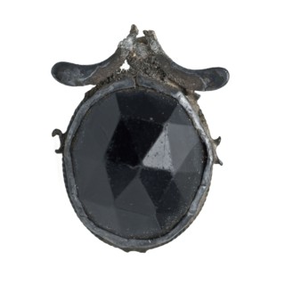 Black, oval cut stone, encased in metal frame, jewelery clothing accessory clothing fragment soil find silver? stone glass metal