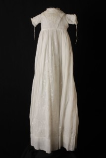 Long flared christening dress of white batiste, V-shaped front and skirt embroidered with fine plumetis, short sleeves